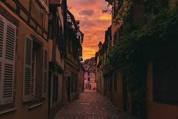 a cobblestone street lined with buildings under a colorful sky